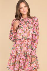 This pink dress features a high neckline, a keyhole cutout at the back of the neck with a button closure, a sheer smocked section at the shoulders, sheer long sleeves with smocked cuffs, and a flowy skirt.