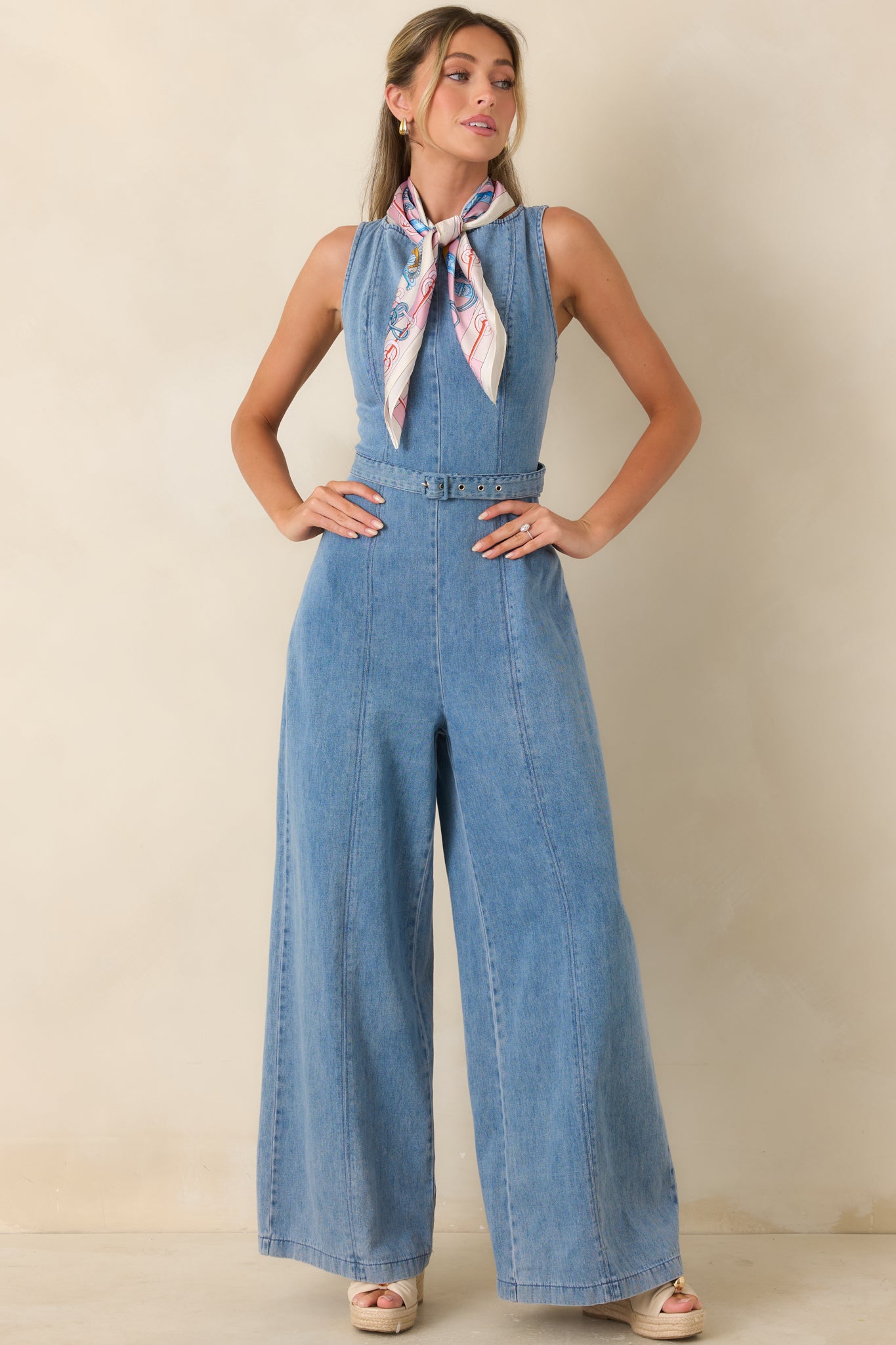 Fitted light wash jumpsuit showcasing a sleeveless cut, clean lines, and a softly structured waist with belt detail.