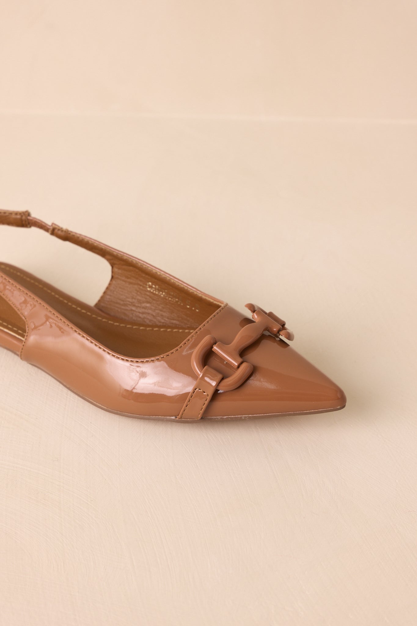 An overhead angled view of the flats on a beige background, focusing on the pointed toe and smooth patent surface.