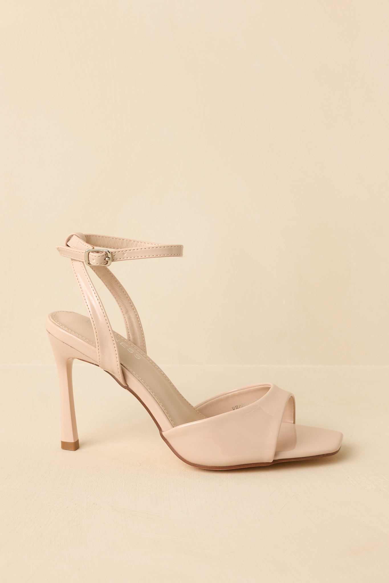 Side angle against a beige background emphasizing the stiletto heel height and ankle strap silhouette.