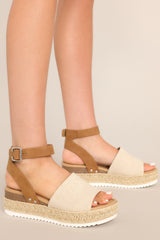 These brown sandals feature a rounded toe, silver hardware, a textured strap over the top of the foot, a contrasting strap around the heel and ankle, and a buckle closure.