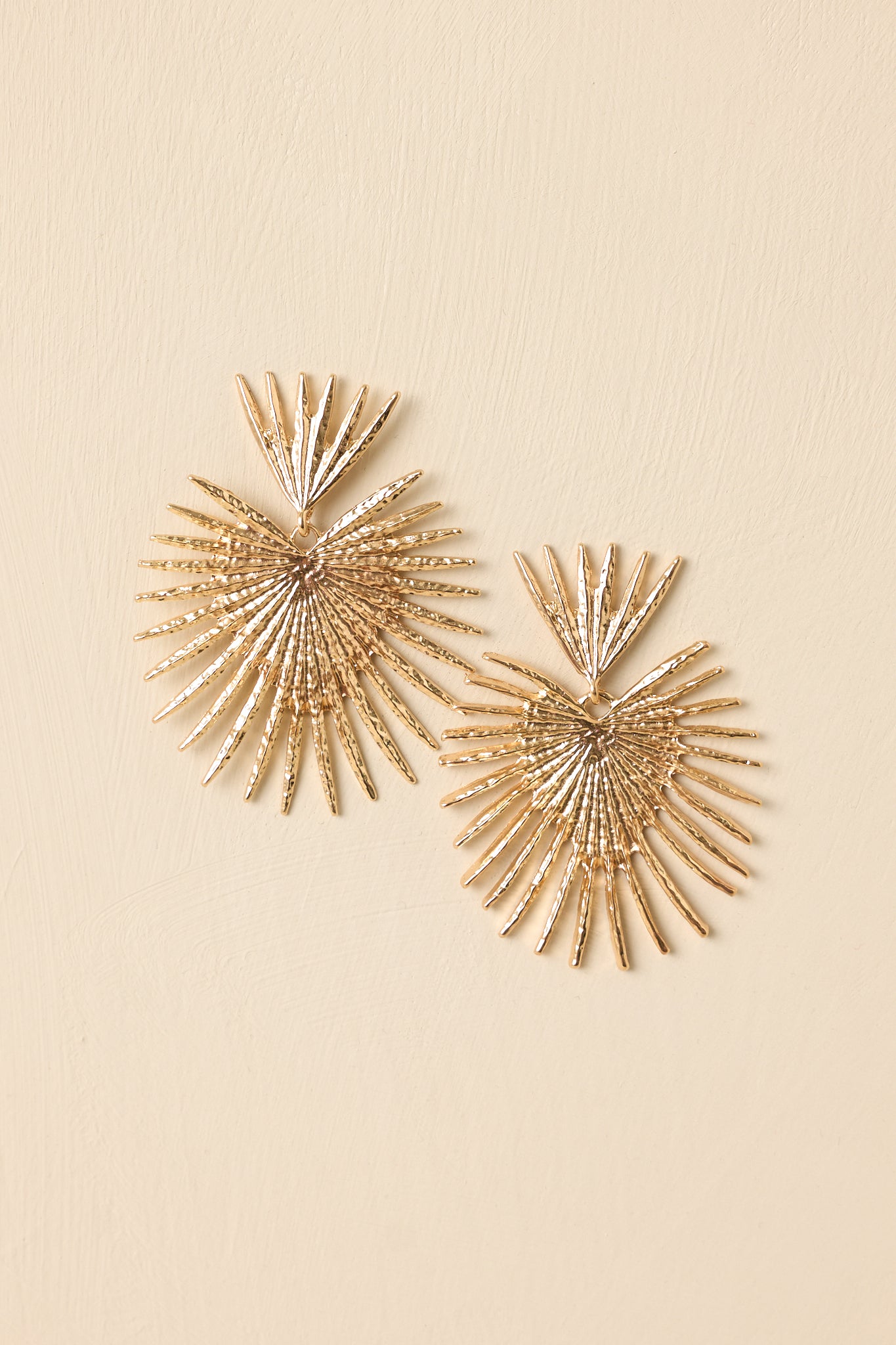 Cropped view of gold-tone statement earrings highlighting the sculptural fan shape and dimensional textured surface.