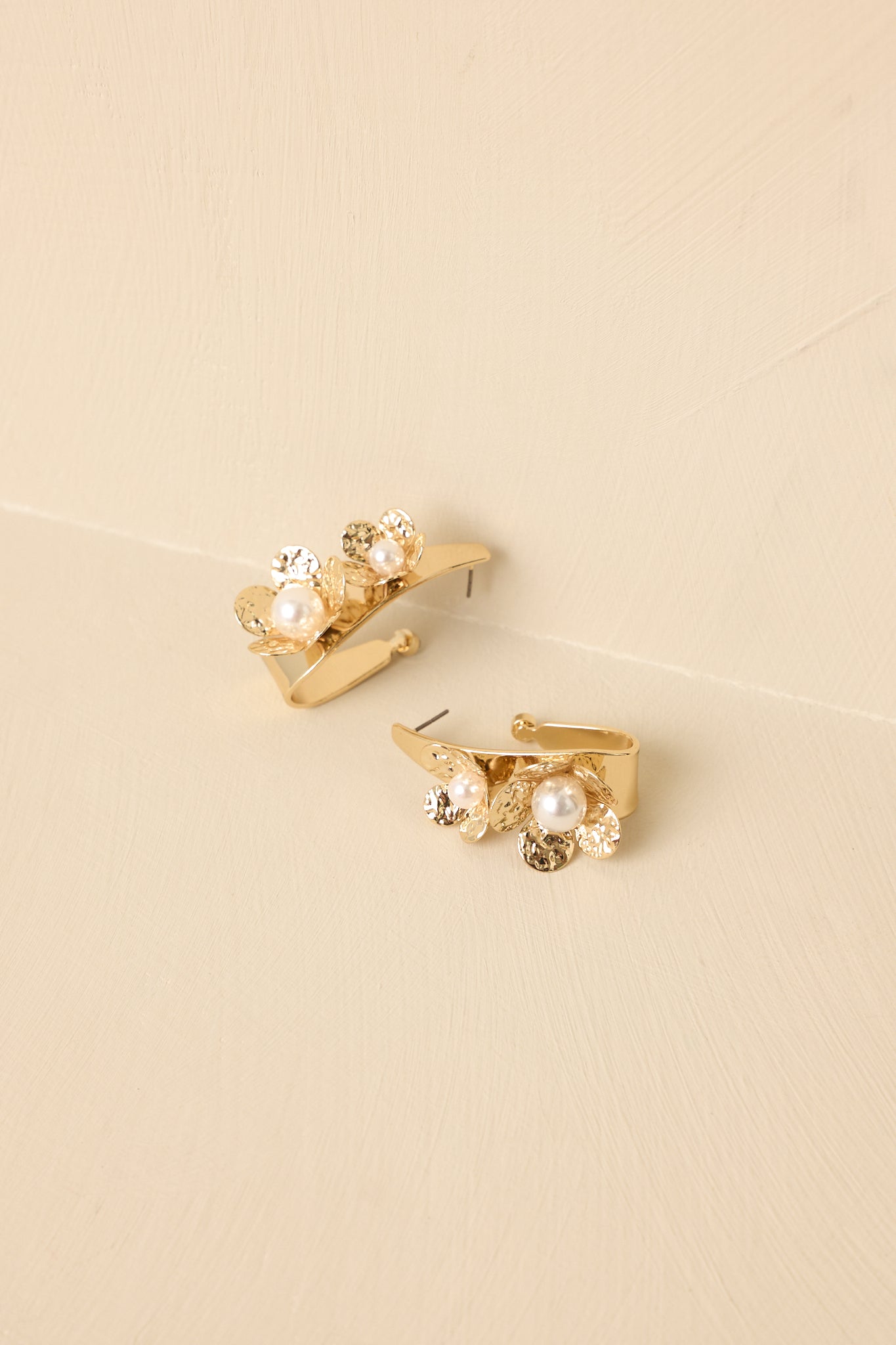 Detailed close-up of the gold-tone floral hoop earrings focusing on the textured petals and pearl accents.