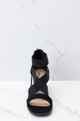 Front view of these heels that feature a rounded toe, a strap across the top of the foot, two stretchy criss-cross straps, and a stretchy strap around the ankle, as well as a block heel and a zipper at the back of the ankle.