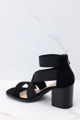 Inner-side view of these heels that feature a rounded toe, a strap across the top of the foot, two stretchy criss-cross straps, and a stretchy strap around the ankle, as well as a block heel and a zipper at the back of the ankle.