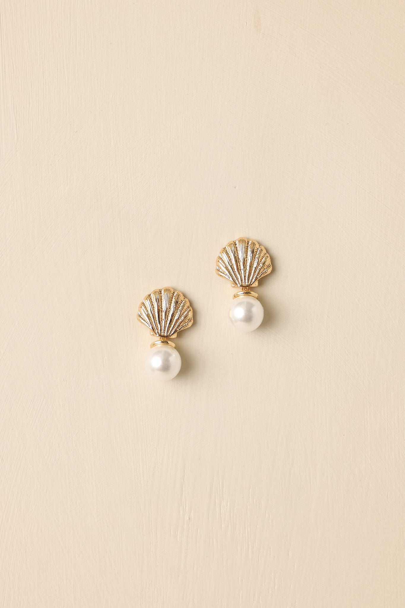 Close-up detail of the textured seashell stud and dangling pearl accent, showing the dimensional metal finish and polished pearl surface.