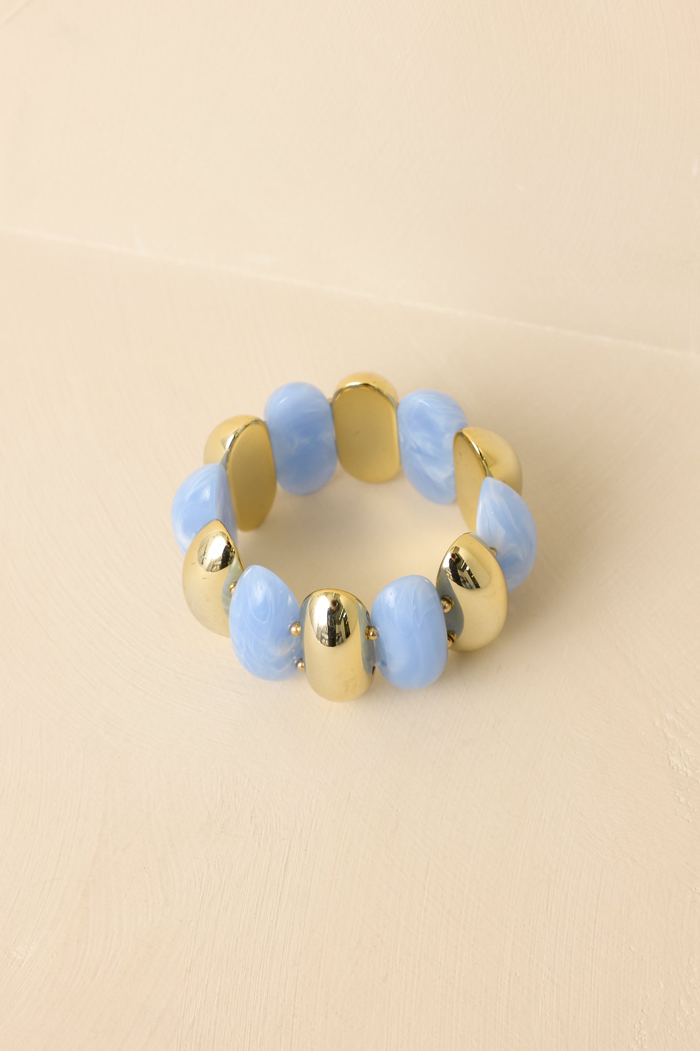 Blue and gold beaded bracelet displayed against a beige background, showcasing the double-row elastic design.