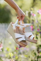 Espadrille sandals with white straps over the top, ankle strap with buckle closure, and wedged heel.