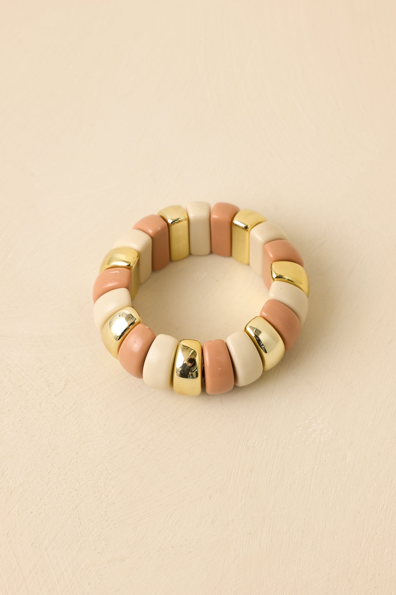 Angled view of statement stretch bracelet on a beige background emphasizing gold bead accents and soft color palette.