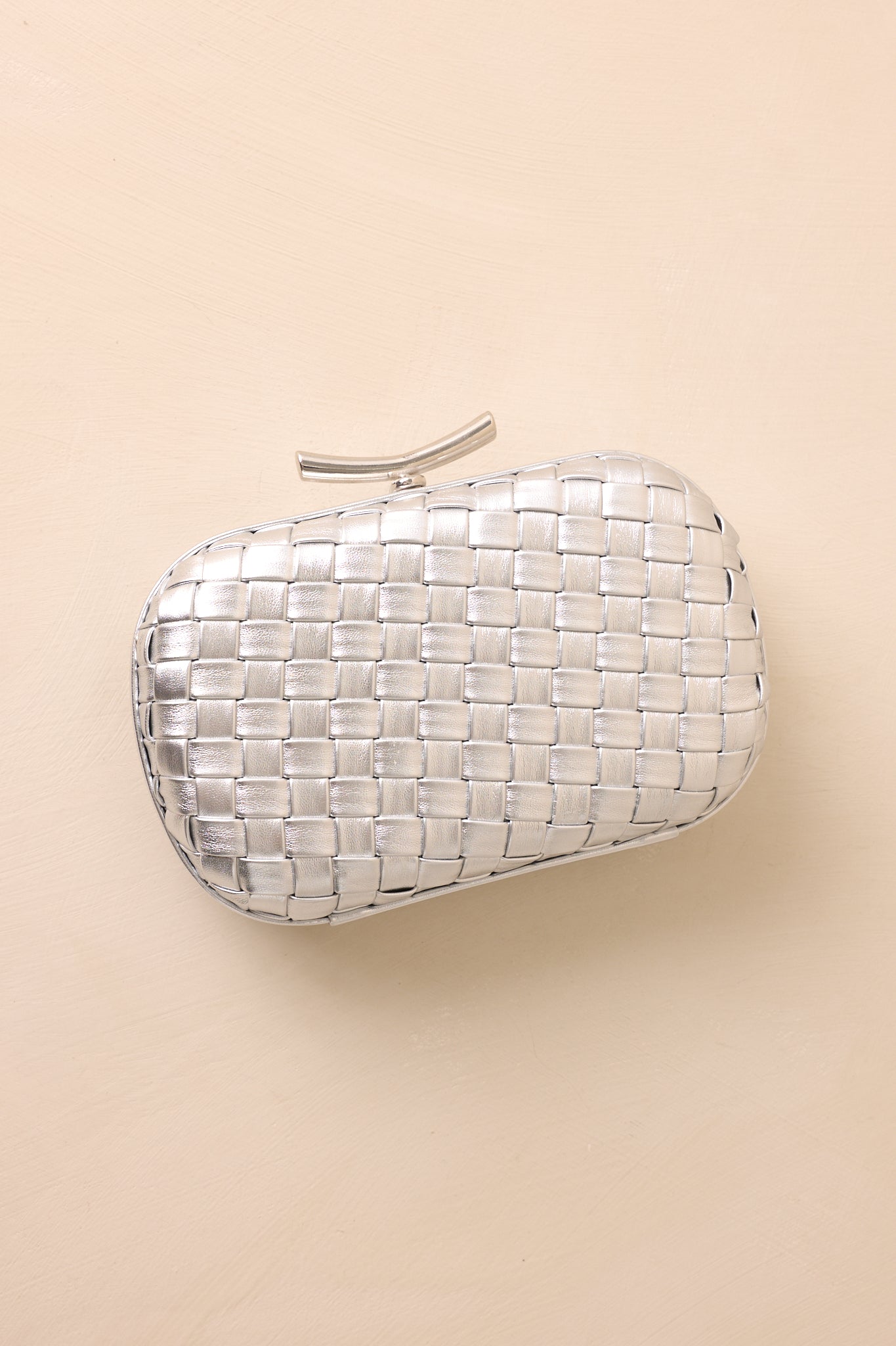 A close-up detail of the silver clutch showing the polished top bar clasp, metallic woven finish, and stitched frame edges.