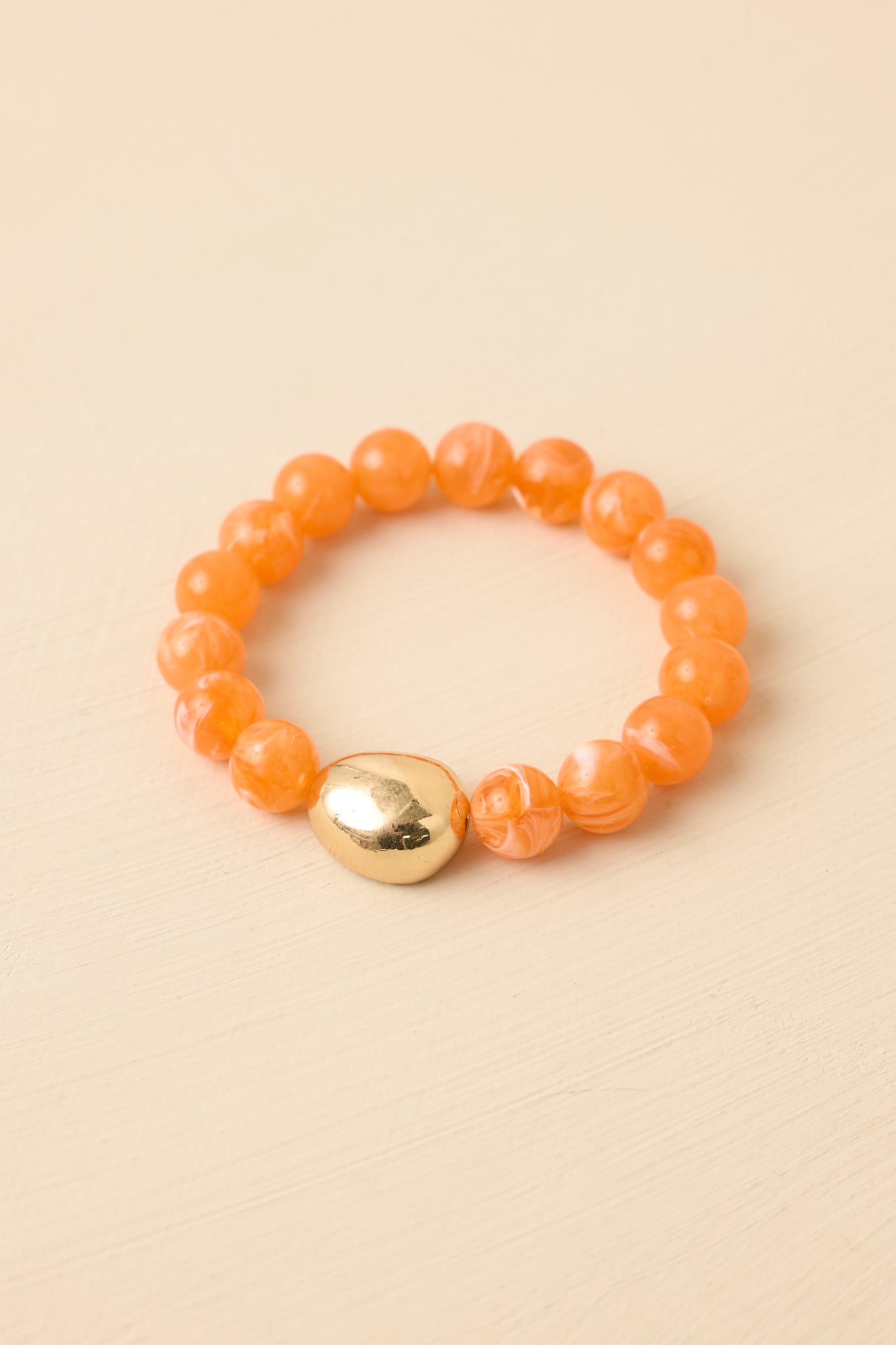 Close-up detail of bracelet showing polished orange beads and central gold-tone accent bead.