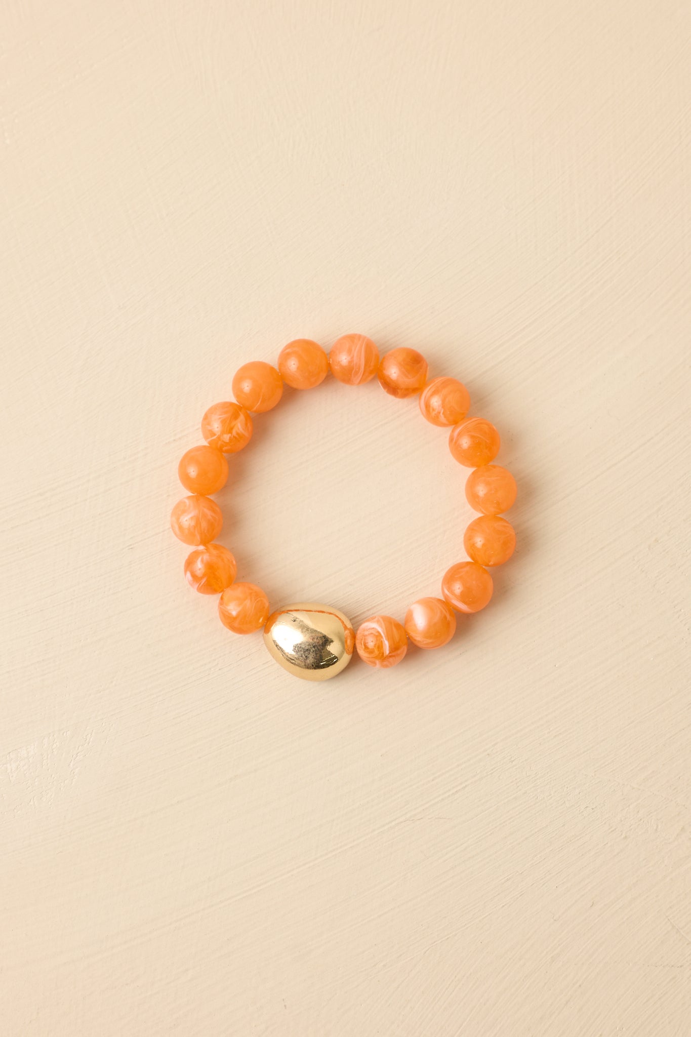 Orange beaded stretch bracelet displayed on beige background emphasizing warm tones and gold accent bead.
