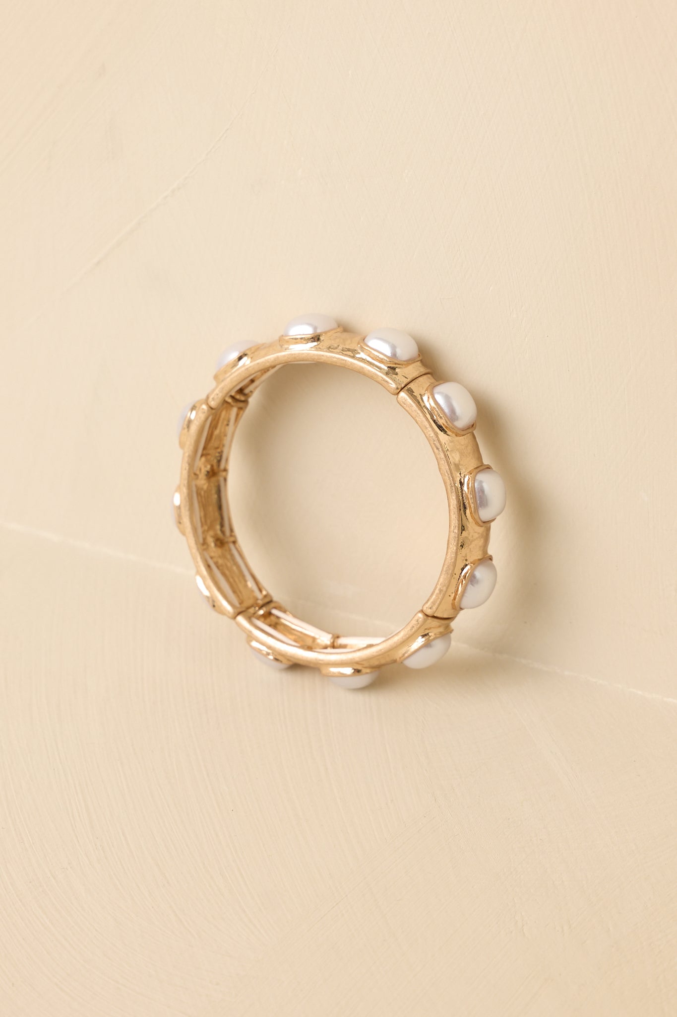 Angled view of the gold metal stretch bracelet on a beige backdrop, showcasing the pearl cabochon detailing across each section.