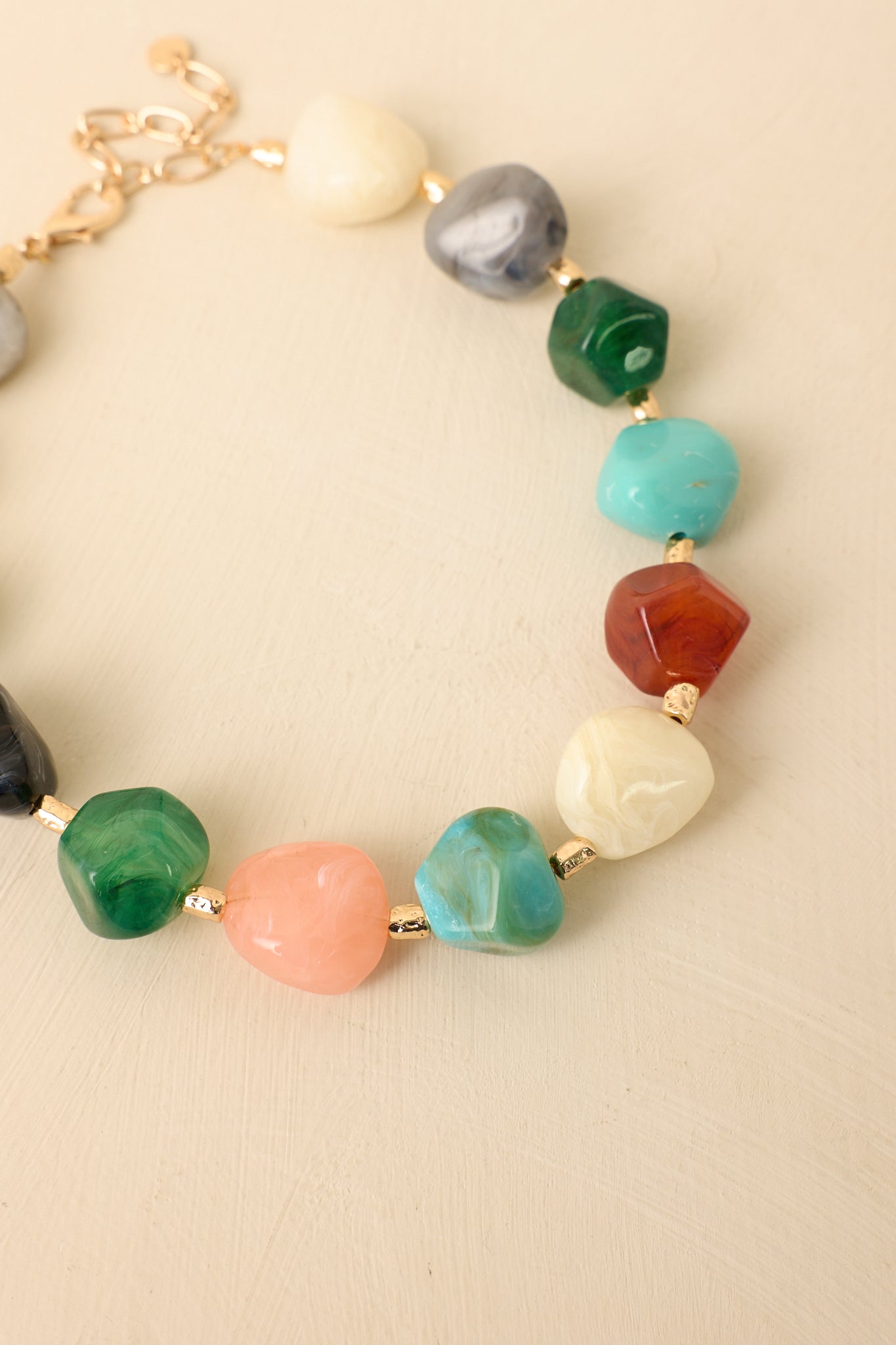 Cropped view of multi-colored gemstone-inspired necklace featuring varied stone shapes separated by gold accent links.