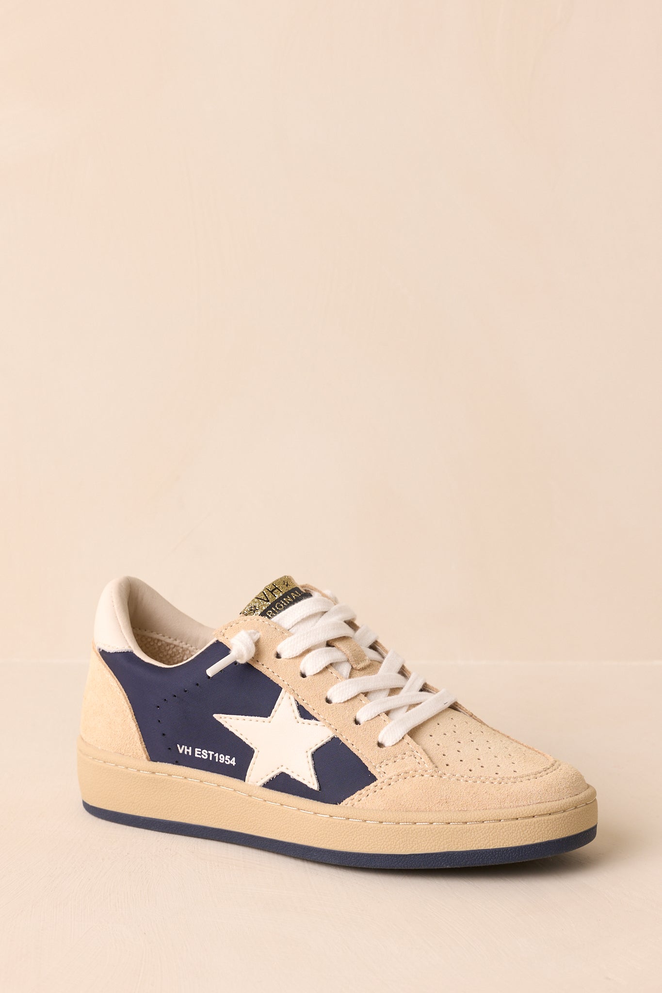 Three-quarter view displaying the cushioned collar, tonal flat rubber outsole, and balanced beige and navy color blocking.