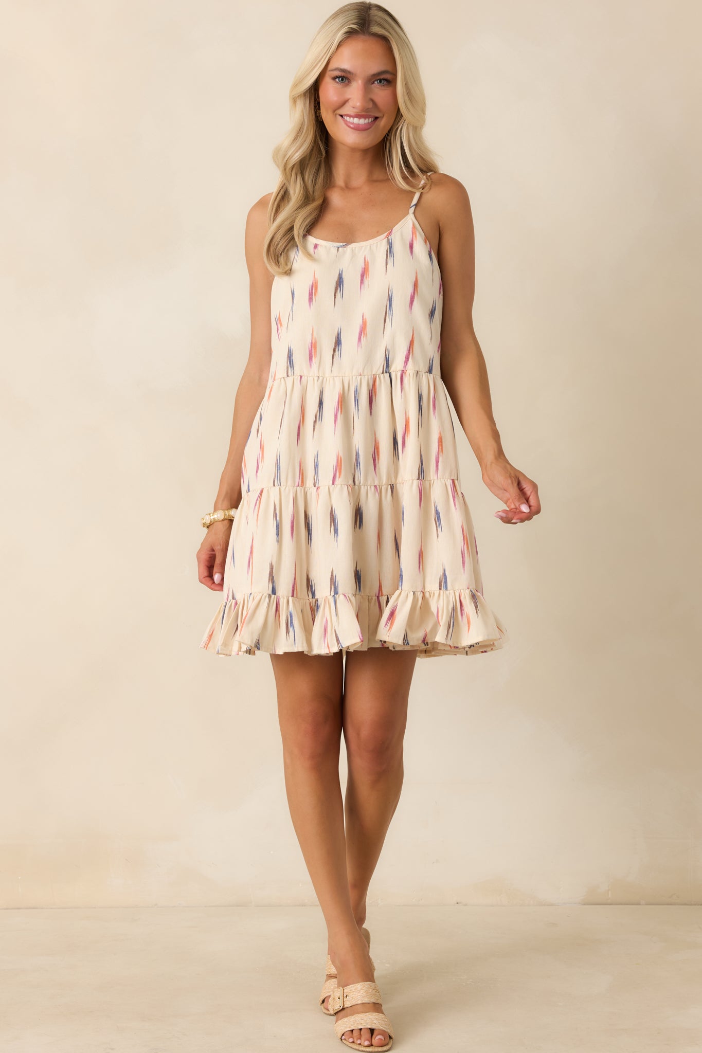 Ivory multi print mini dress featuring adjustable spaghetti straps, a scoop neckline, and a flowy tiered silhouette.