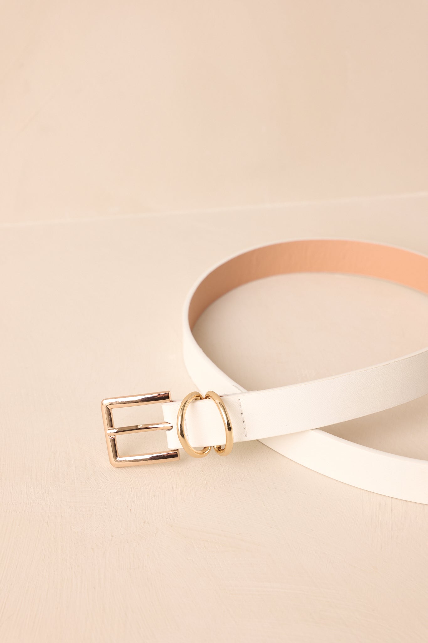 Close-up of the white faux leather belt displaying the polished gold-tone buckle, double metal loops, and texture detail.