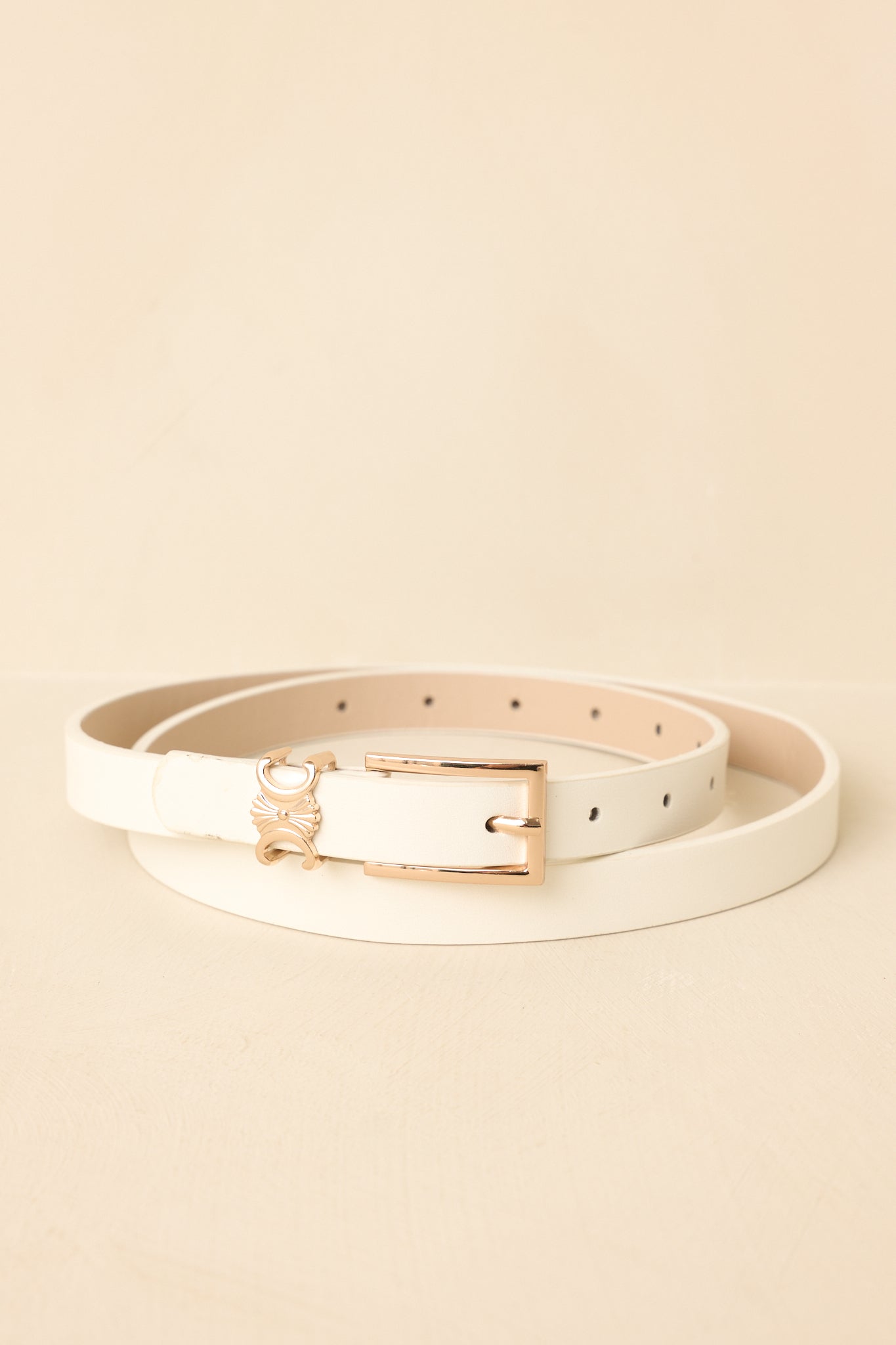 Close-up of white belt showing gold-tone buckle, smooth leather texture, and narrow strap.