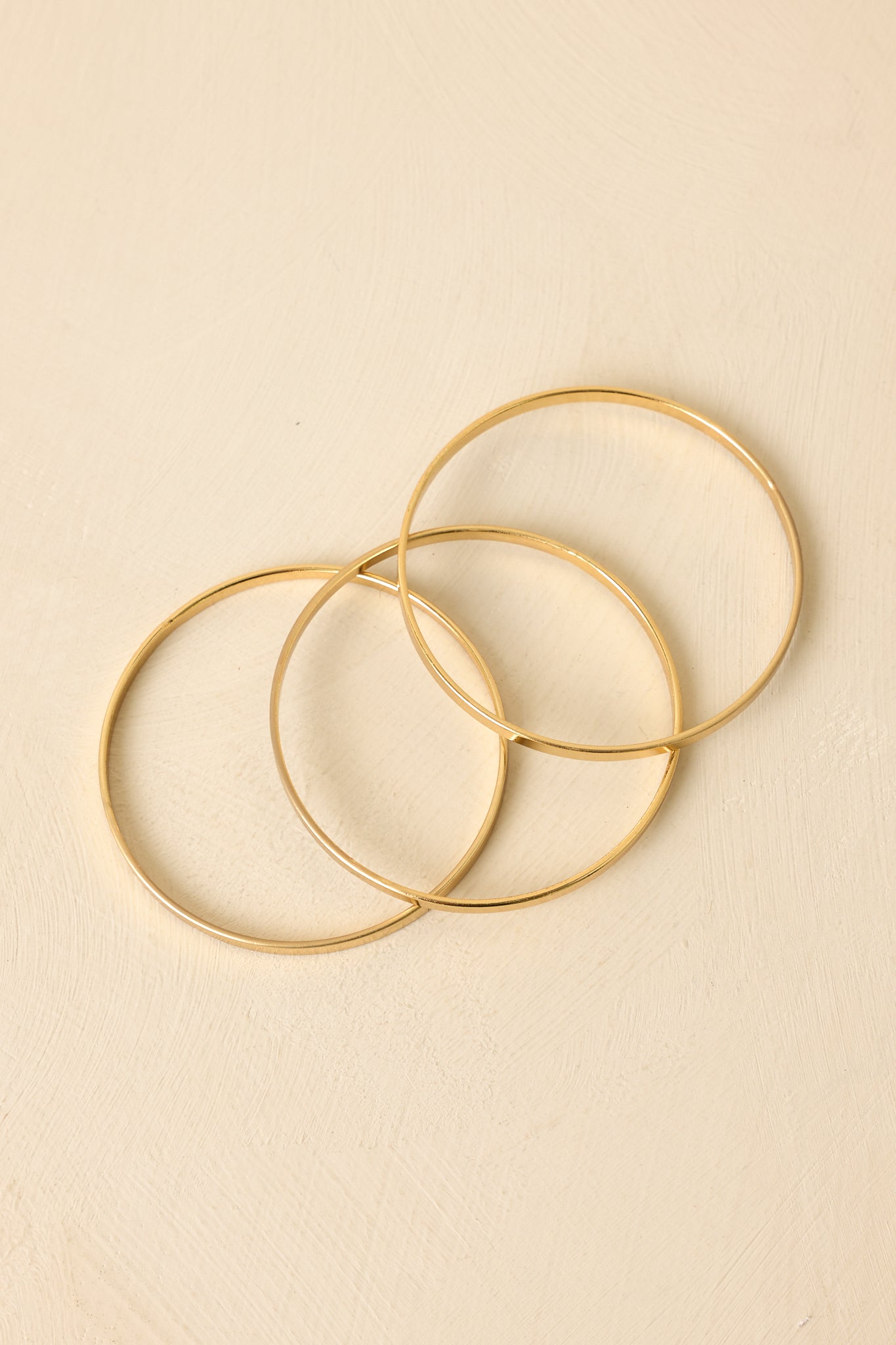 Front view of smooth gold-tone bangles set against neutral beige, emphasizing minimalist layered design.