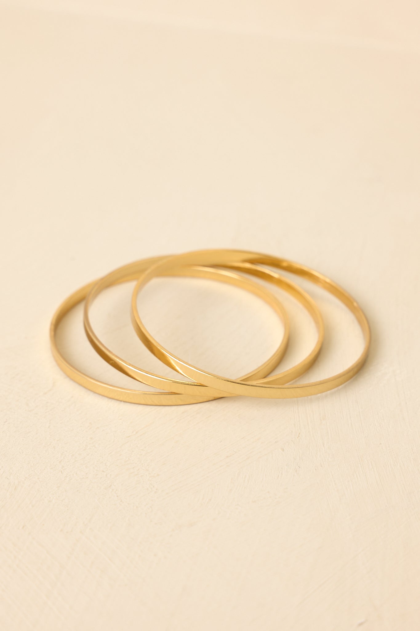 Close-up of gold bangle set showing polished surface, lightweight construction, and stackable design for modern elegance.