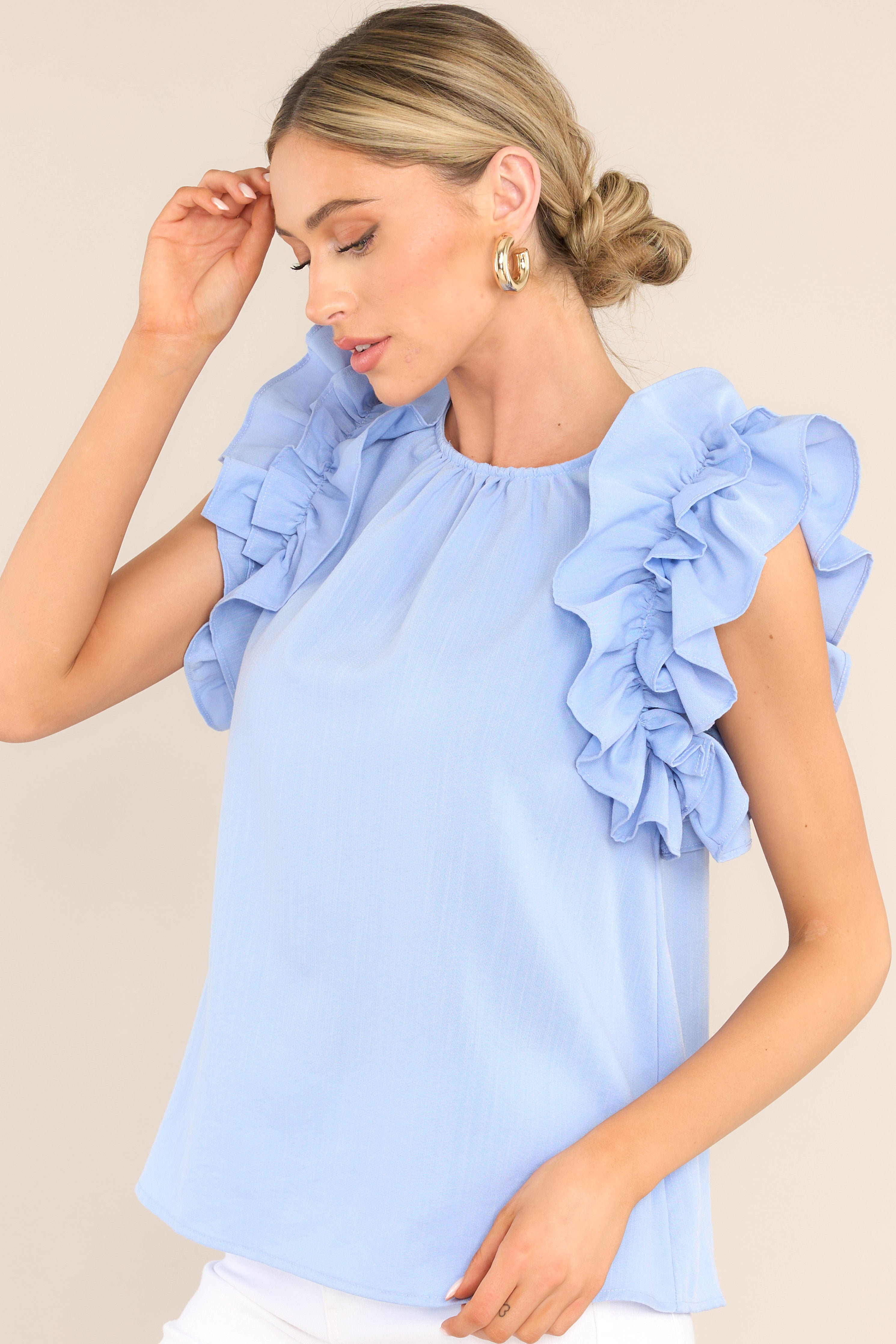 This blue top features a high crew neckline, a keyhole with a button closure at the back of the neck, and ruffled shoulder detailing. 