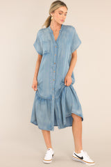 This chambray dress features a v-neckline, a functional chest pocket, a button front, functional hip pockets, a tiered design, and a front slit. 