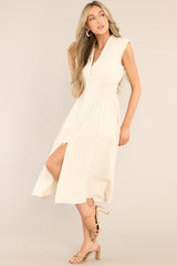Front view of this dress that features a deep v-neckline, shoulder padding, a functional zipper front, a fully smocked waist, functional pockets, and a front slit. 