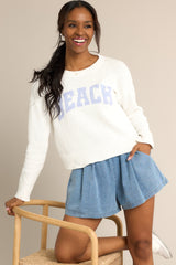 This white sweater features a ribbed crew neckline, varsity style wording across the chest, and ribbed cuffed long sleeves. 