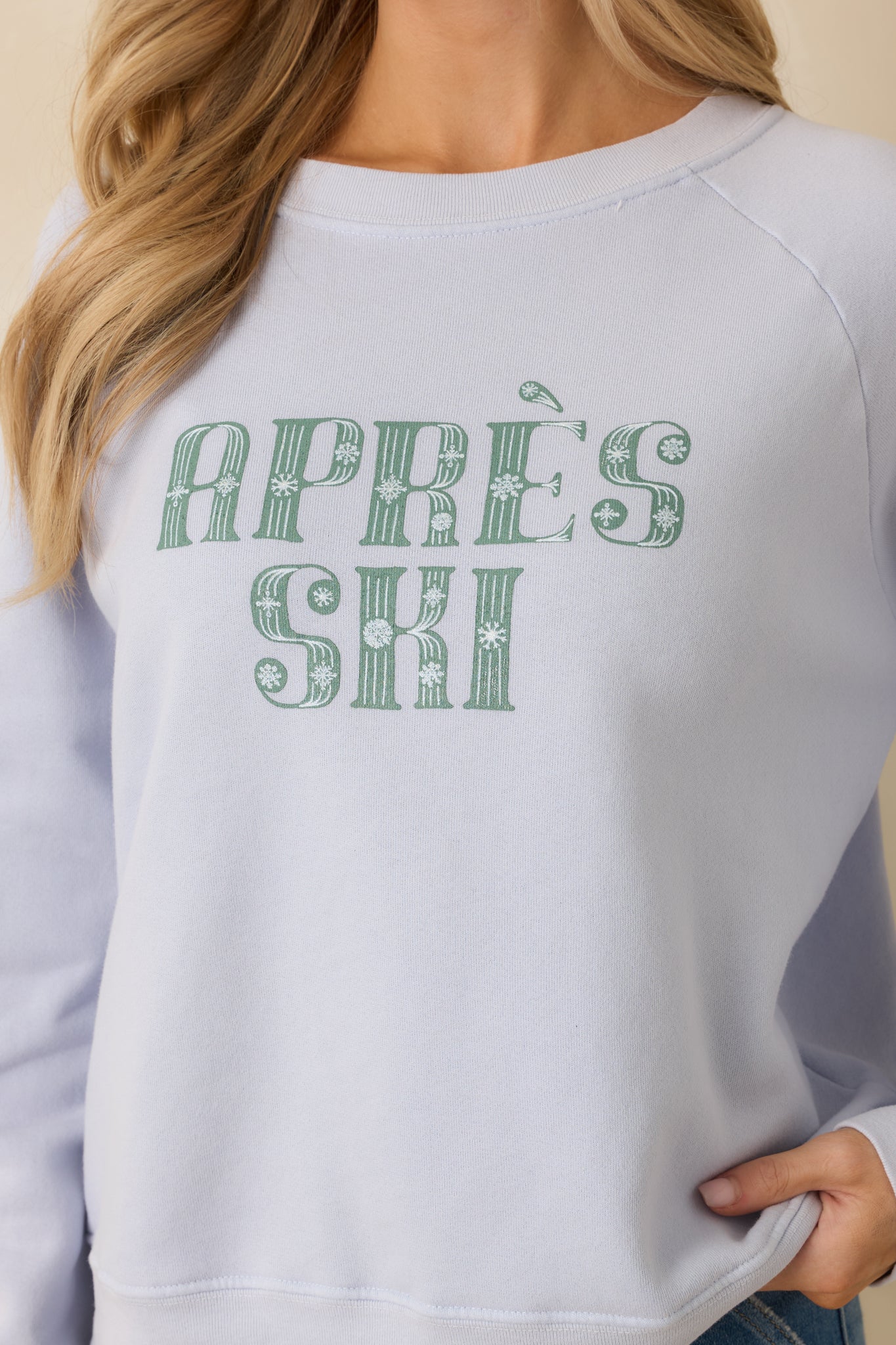Close detail of the light blue sweatshirt showcasing the textured knit cotton blend and bold “Après Ski” lettering.