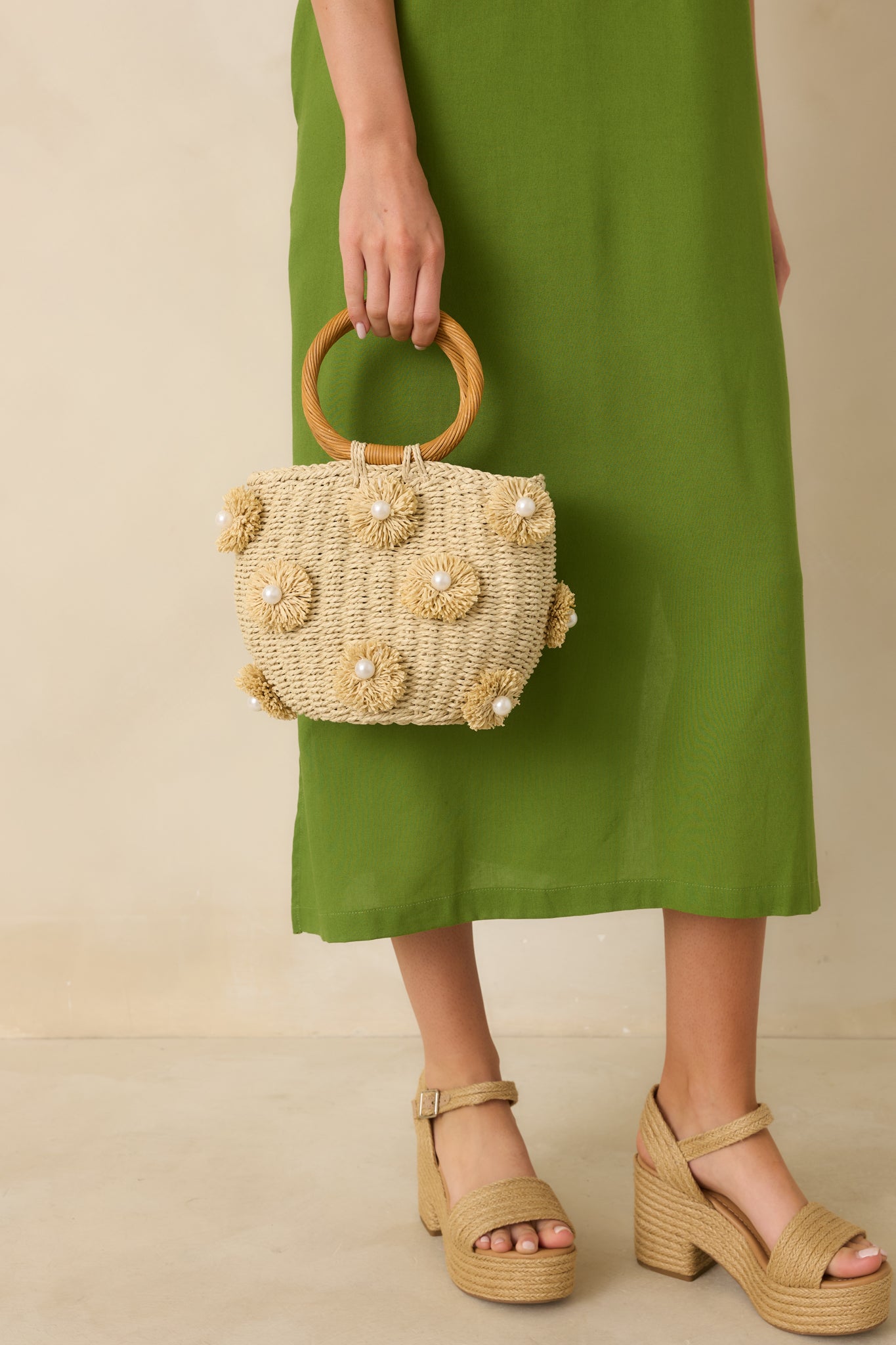 Front view of the natural woven handbag showing the textured woven body, structured silhouette, and round top handle.