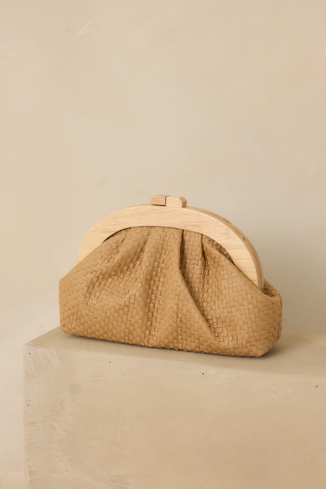 Cropped front view emphasizing the woven texture, wooden top frame, and magnetic clasp closure of the tan clutch.