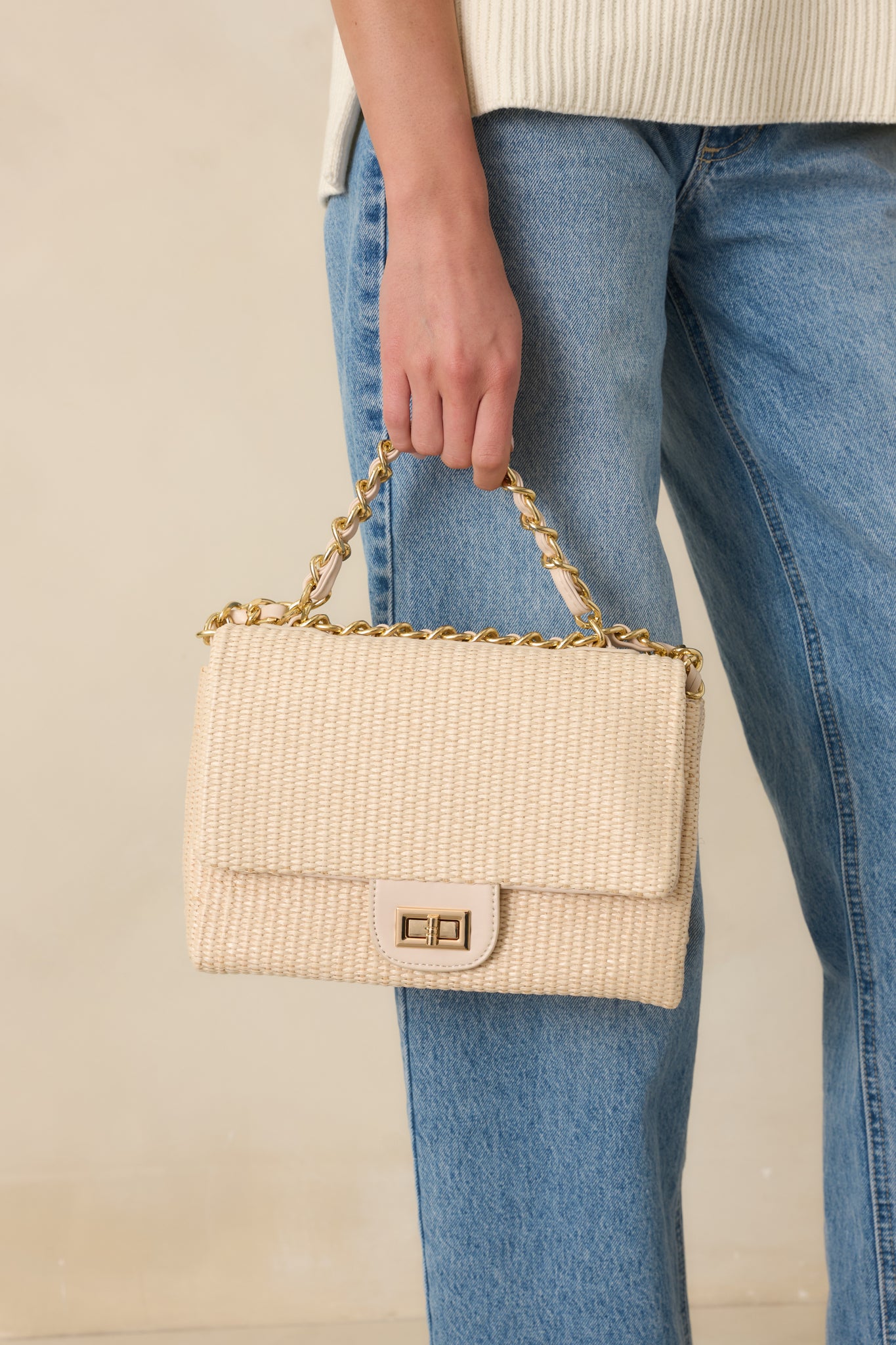 Cropped front view emphasizing the woven texture and polished gold-tone turn-lock closure of the structured ivory handbag.