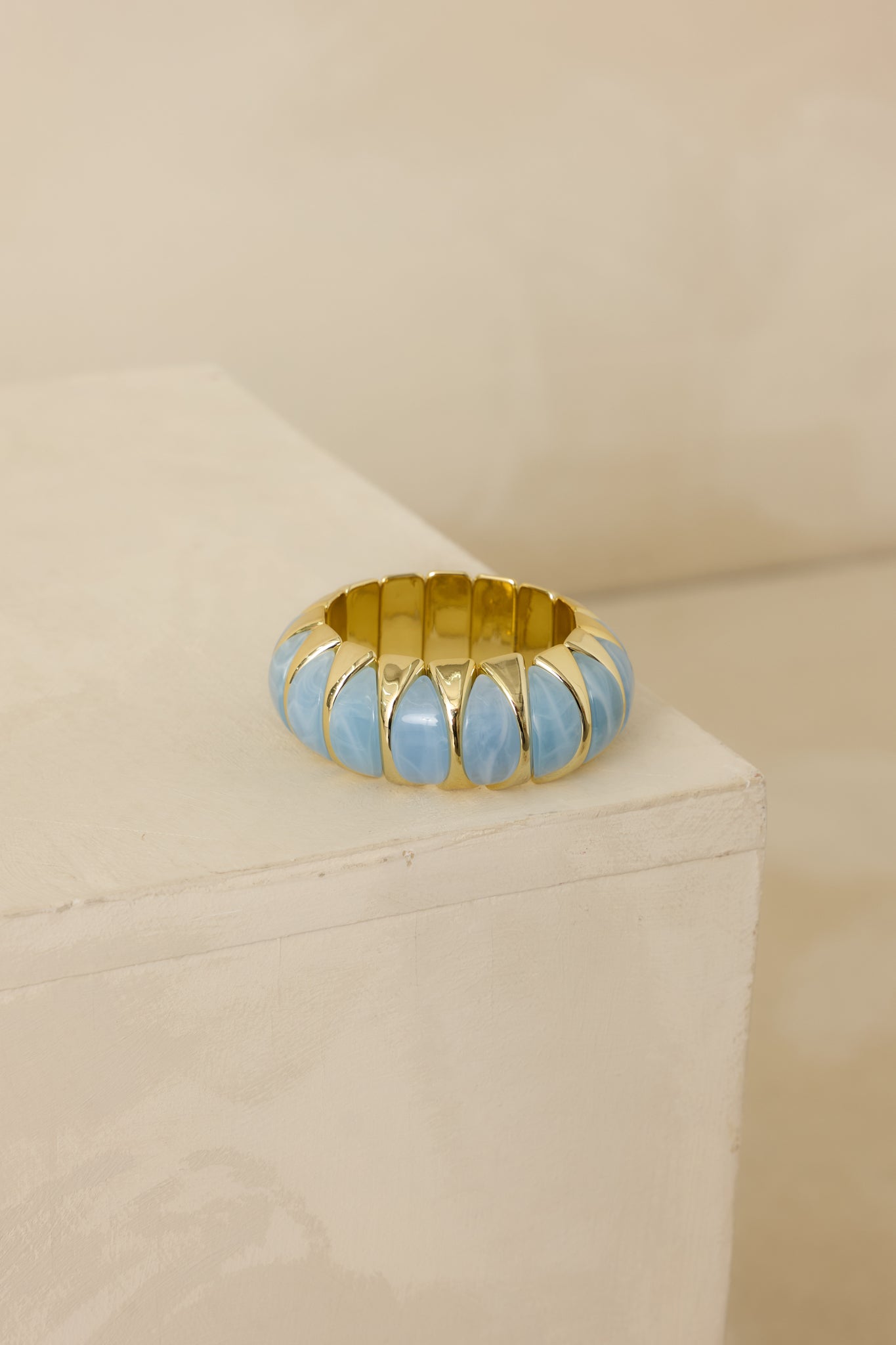 Cropped view of the light blue and gold stretch bracelet showing sculptural blue beads framed by polished gold links.