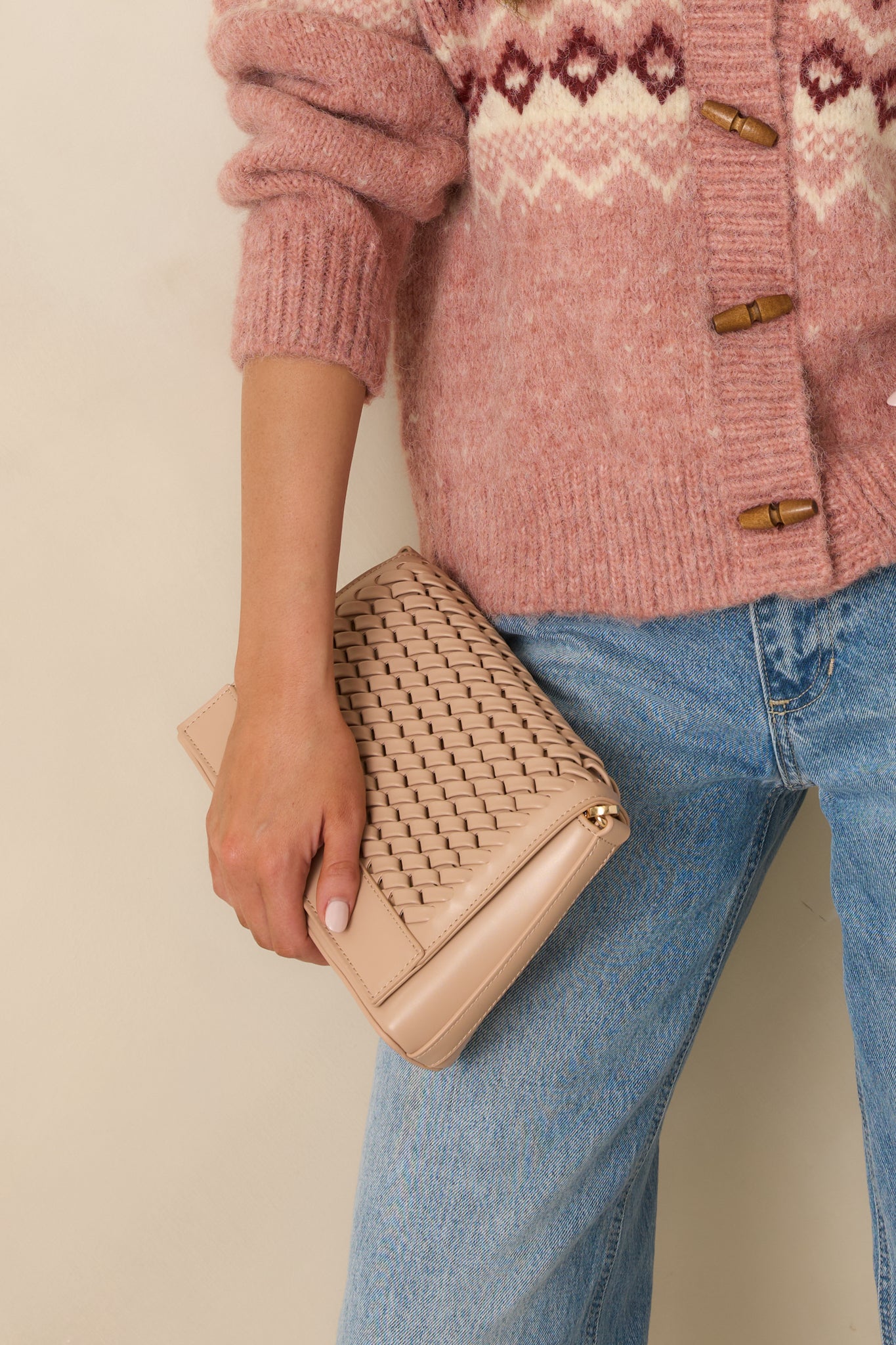 Cropped detail highlighting the front flap design and smooth woven finish of the beige faux leather handbag.
