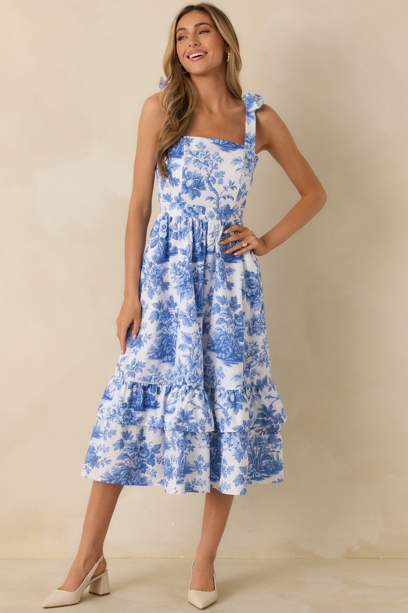 Blue and white printed midi dress designed with a structured bodice, tiered skirt, and charming shoulder bows.