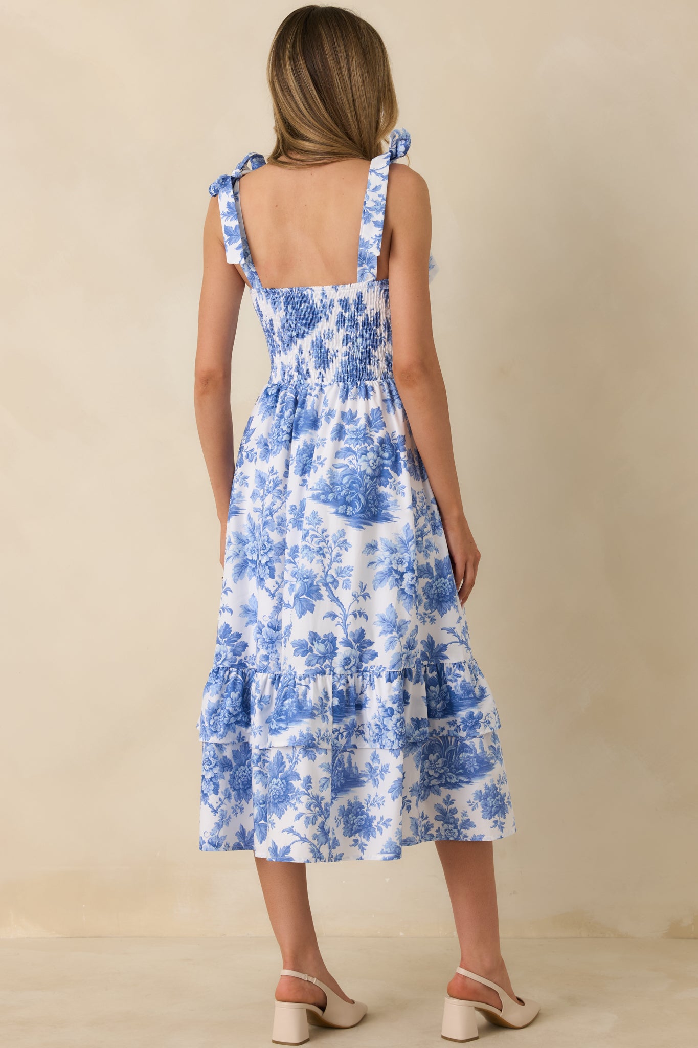 Rear view of the blue and white floral midi dress highlighting the smocked back panel and the flowy tiered skirt.