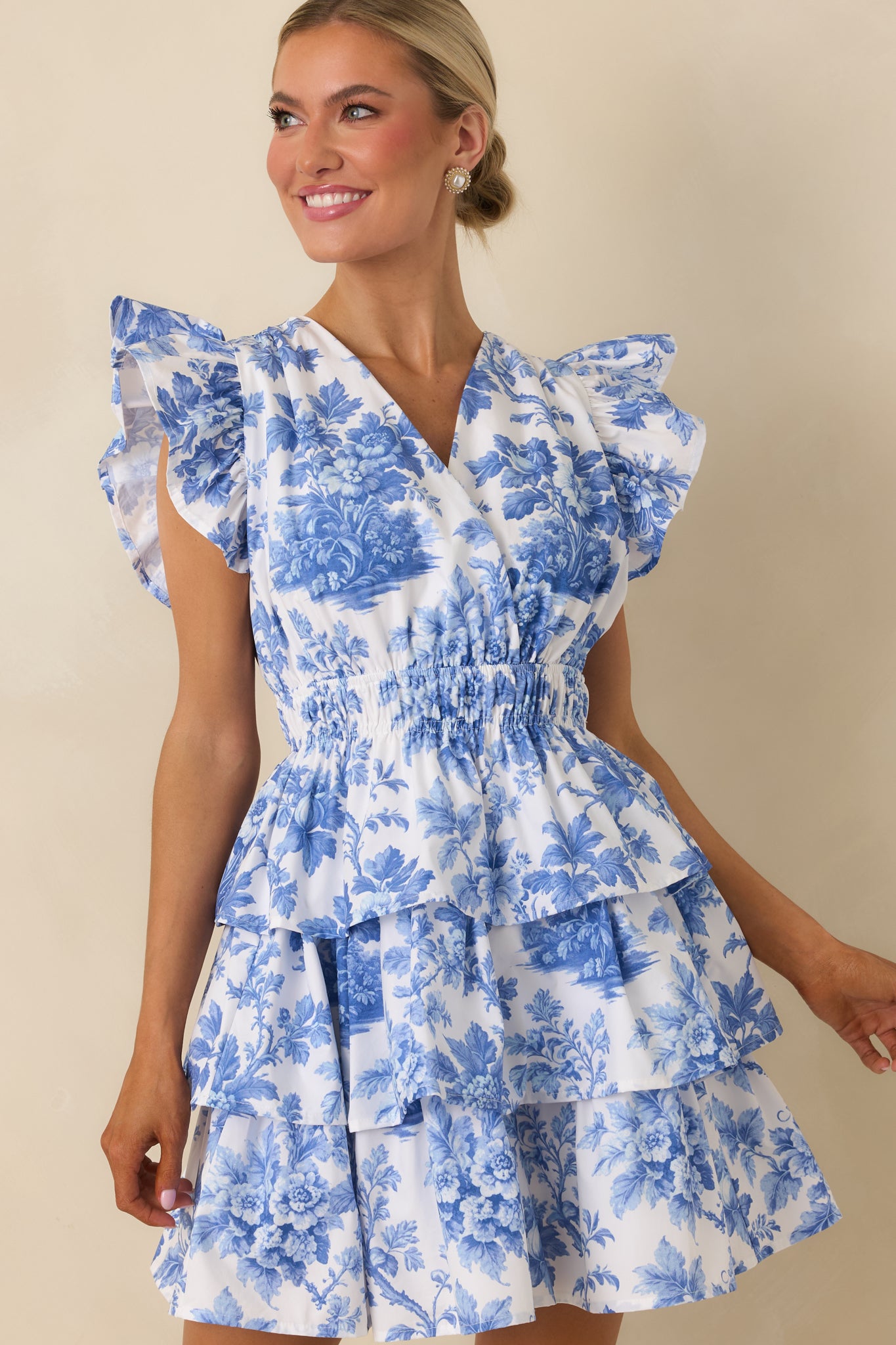 Close look at flutter sleeves, V-neckline, and smocked waist of blue and white floral mini dress.