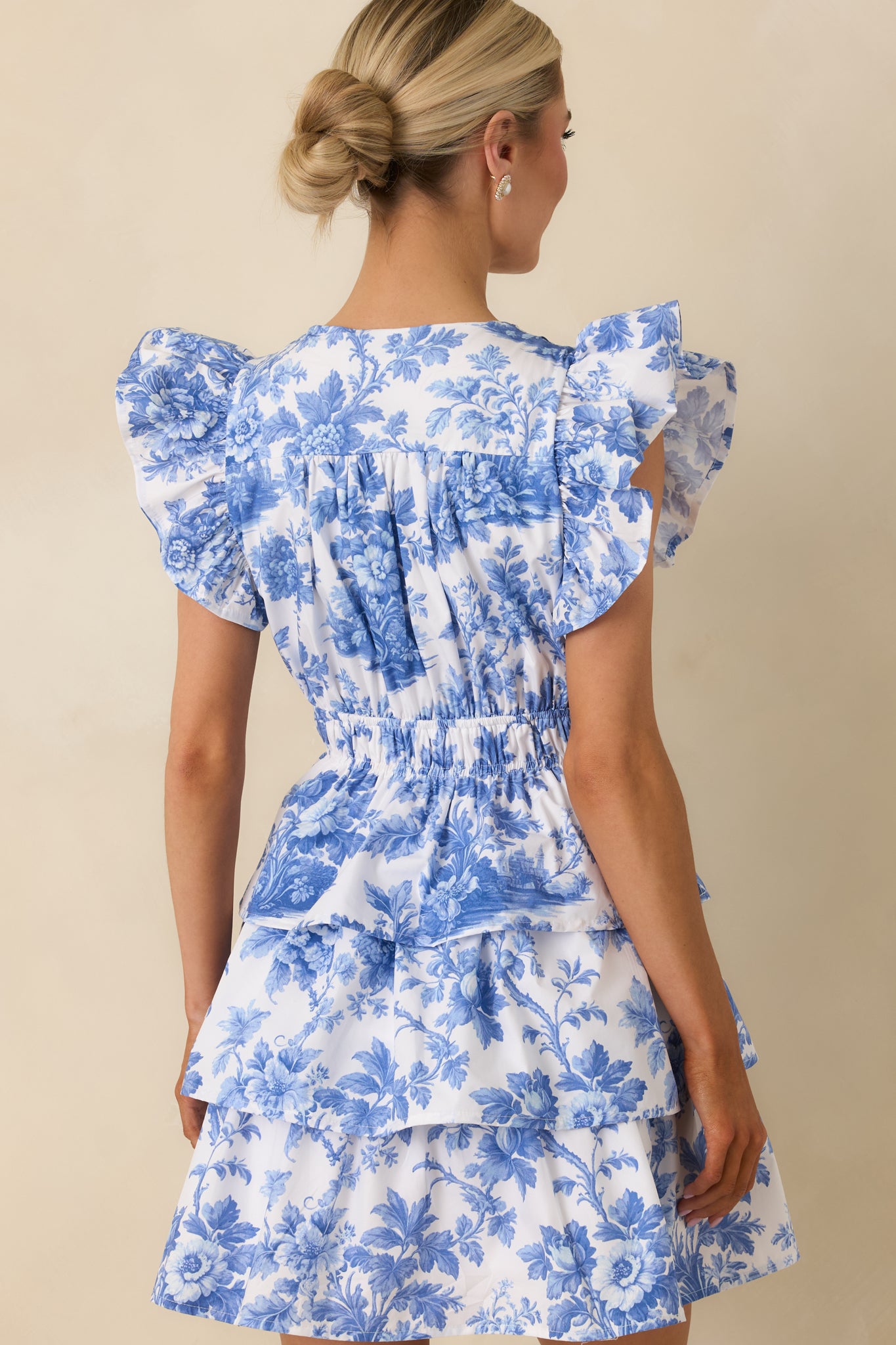 Rear view of blue floral mini dress revealing smocked elastic waist, flutter sleeves, and tiered skirt with structured fit.