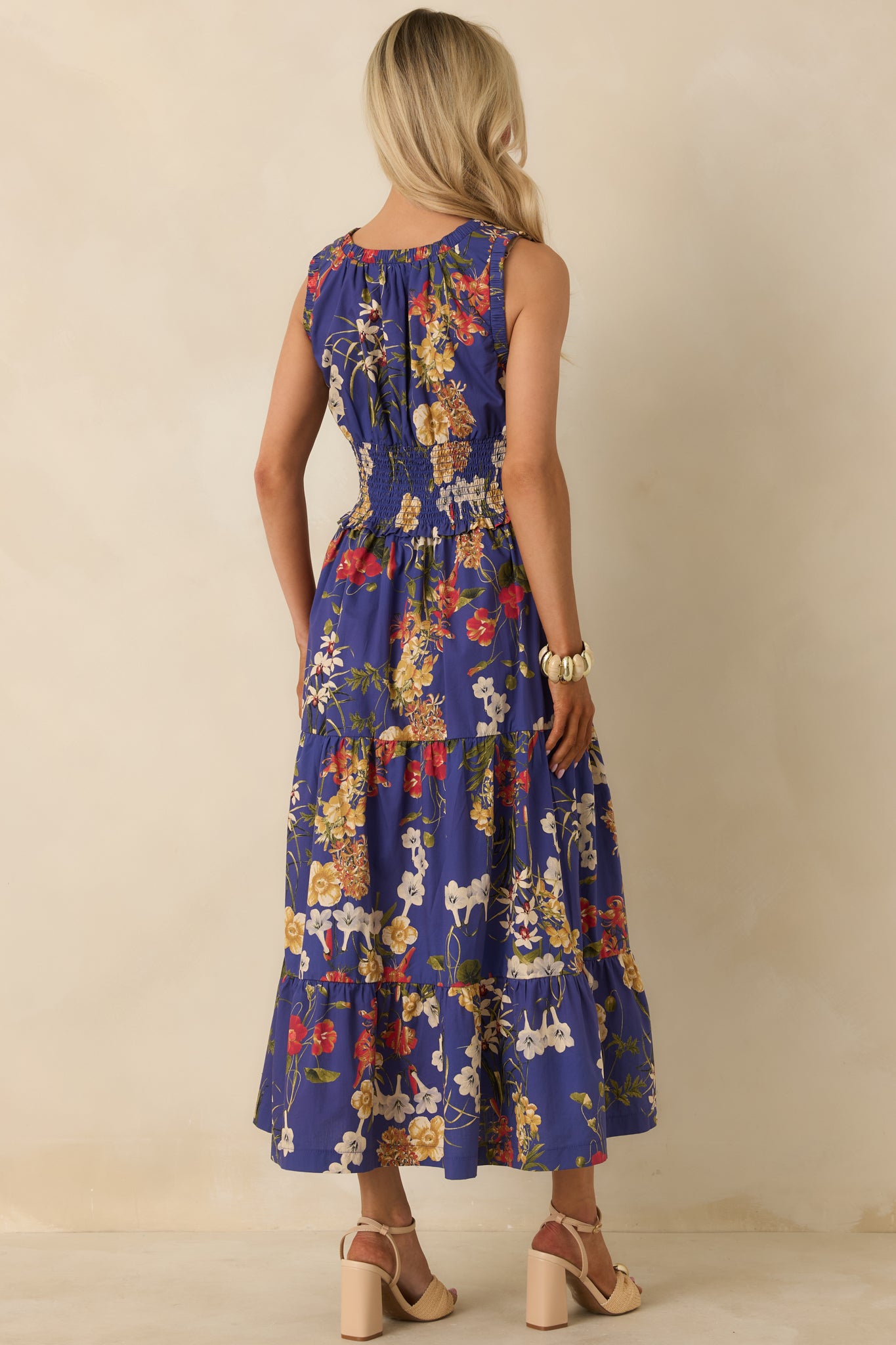 Rear view of cobalt blue maxi dress highlighting smocked waistband, sleeveless design, and flowing tiered skirt with floral pattern.