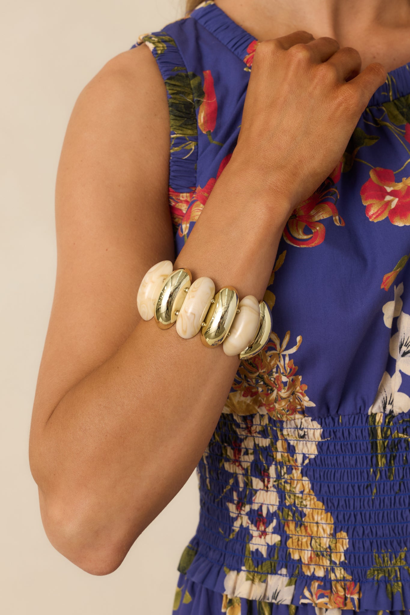 Beige and gold statement bracelet with alternating smooth stone-like beads and shiny gold beads arranged on two stretch rows.