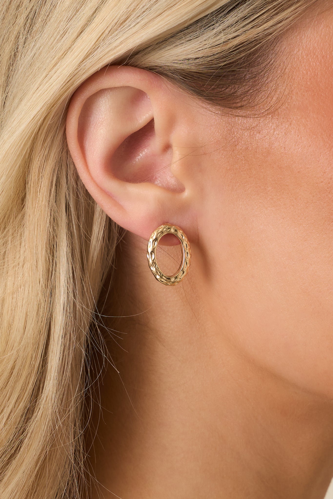 Close-up detail of gold-tone oval stud earrings showing the lightly textured surface and post-back closure.