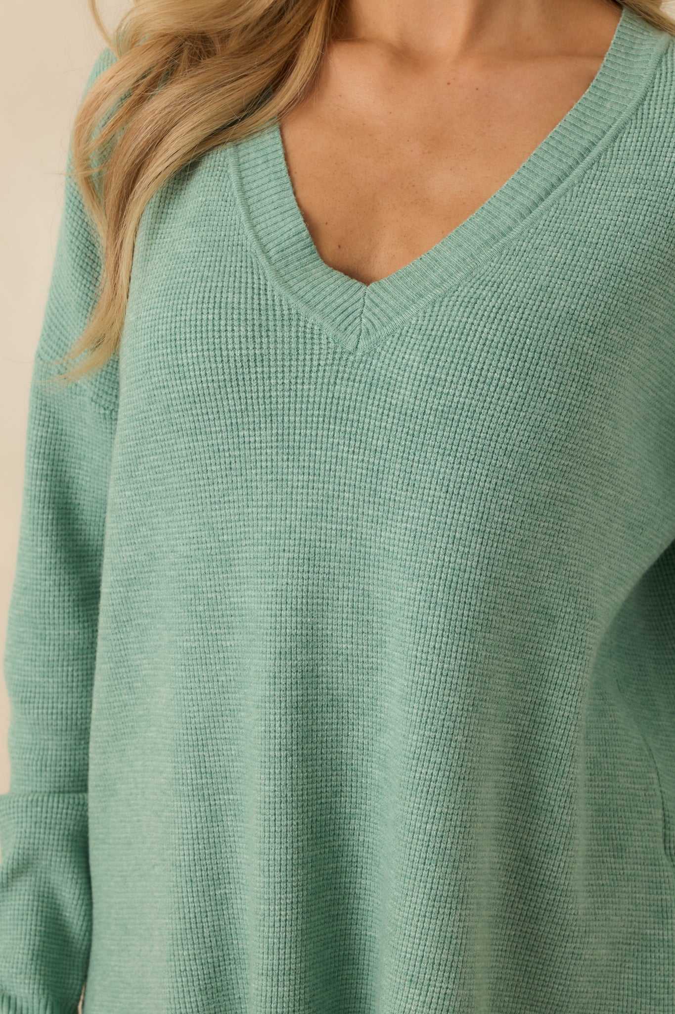 Detailed look at the split hem bottom, ribbed cuffs, and soft knit fabric of the light green sweater.