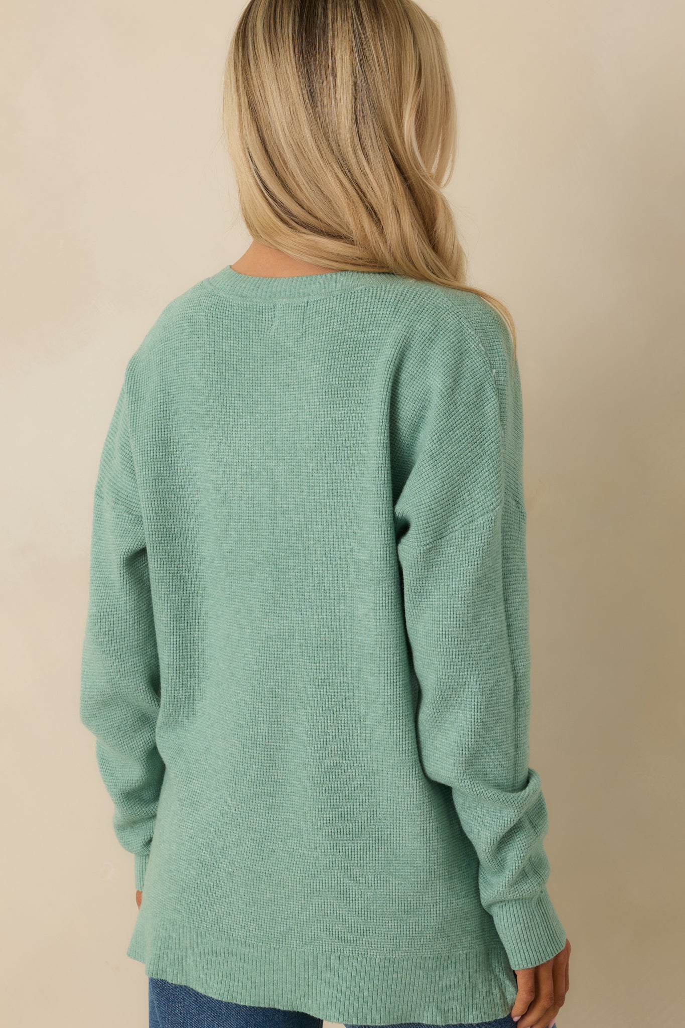 Rear view of the light green sweater showing the relaxed fit, long sleeves, and split hem design.