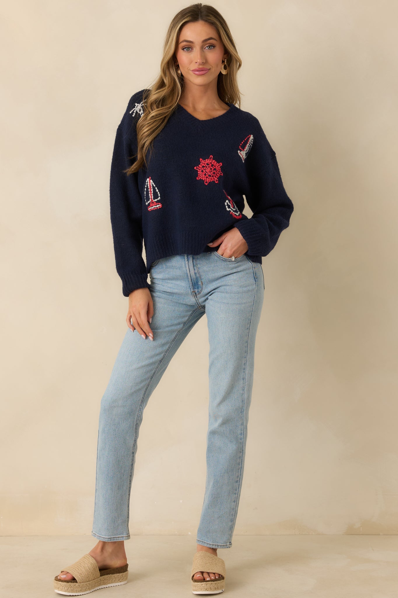 Navy knit sweater with a relaxed fit, V-neckline, and long sleeves, featuring multi-color nautical embroidery throughout.