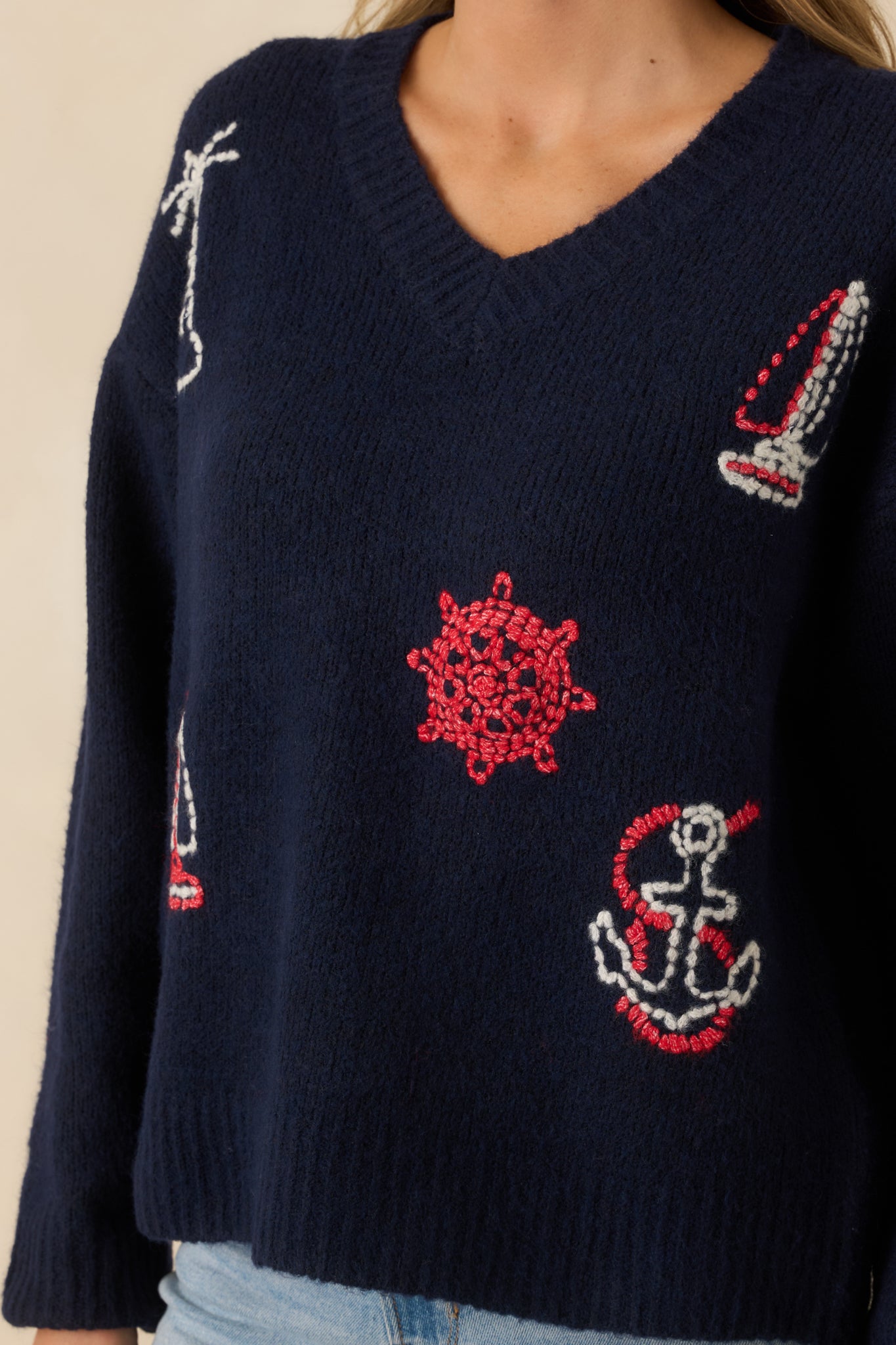 Detailed view of navy knit sweater showing multi-color nautical embroidery, V-neckline, and ribbed trim at neckline, cuffs, and hem.