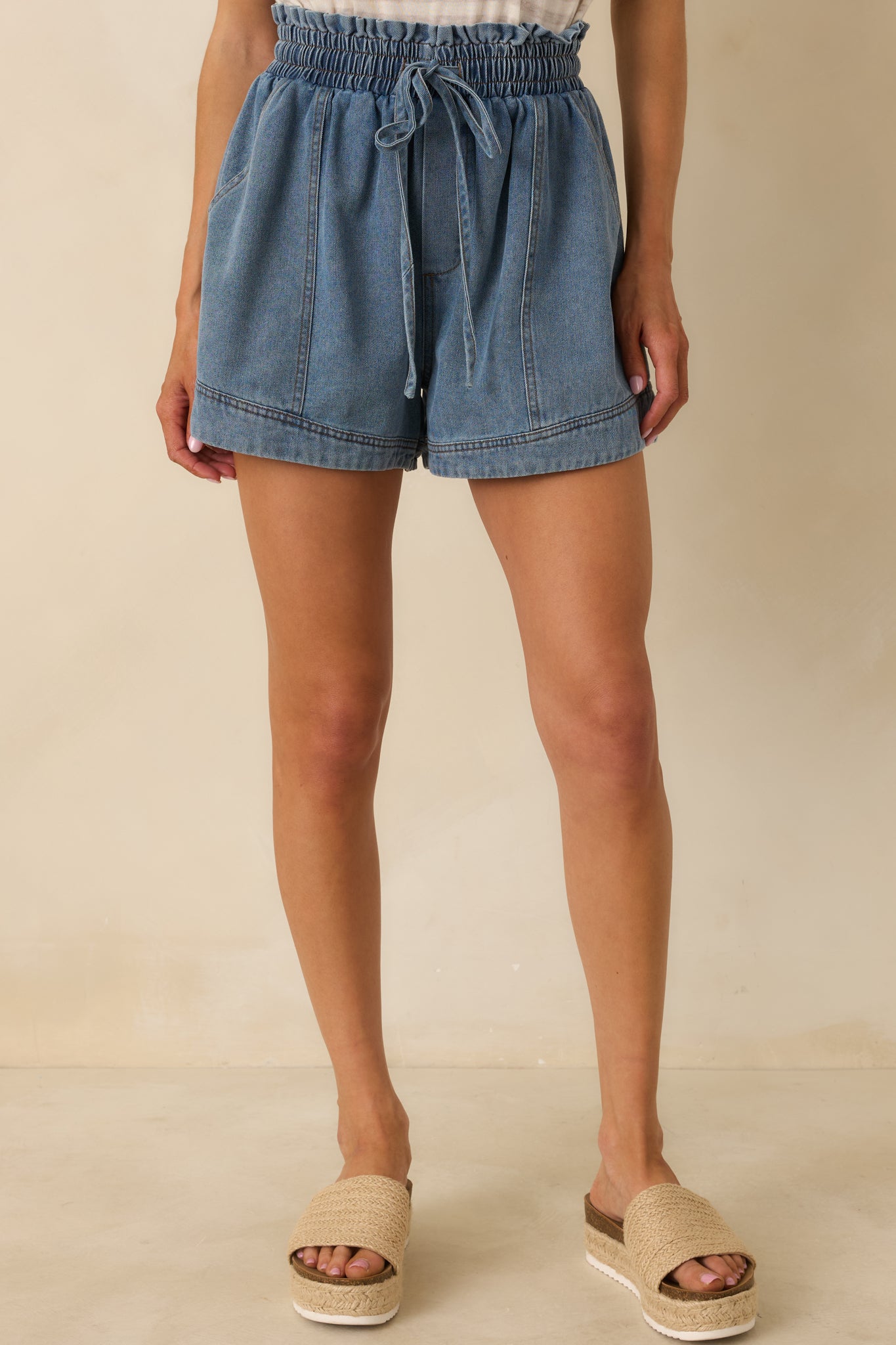 Midsection view showing relaxed fit and faux zipper detail of medium wash denim shorts.