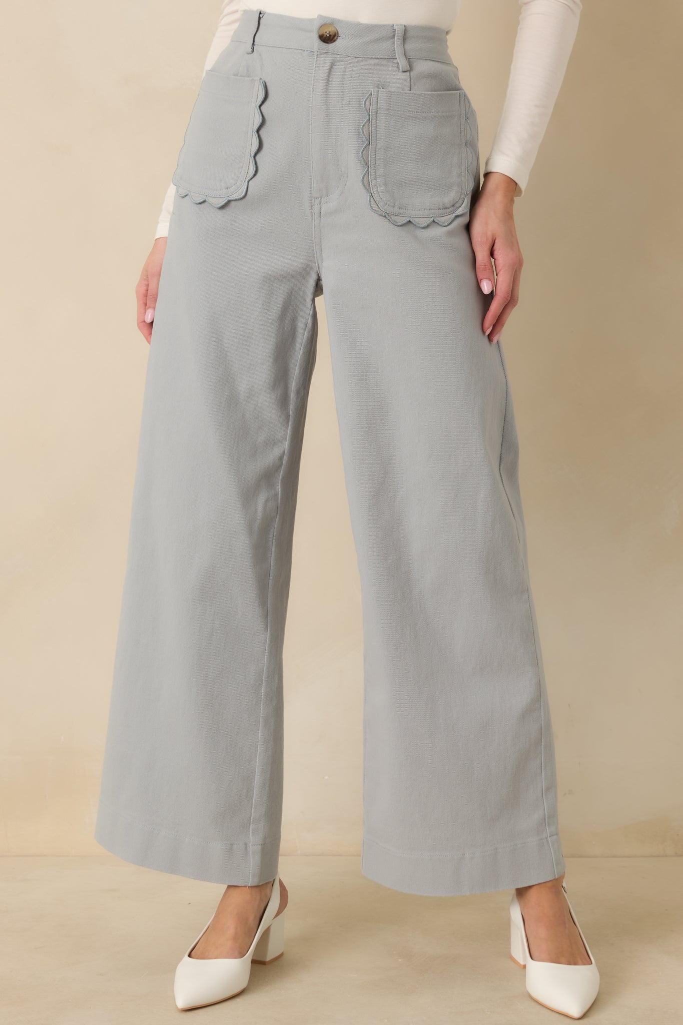 Close crop highlighting high-rise waistband and neat front button of blue pants.