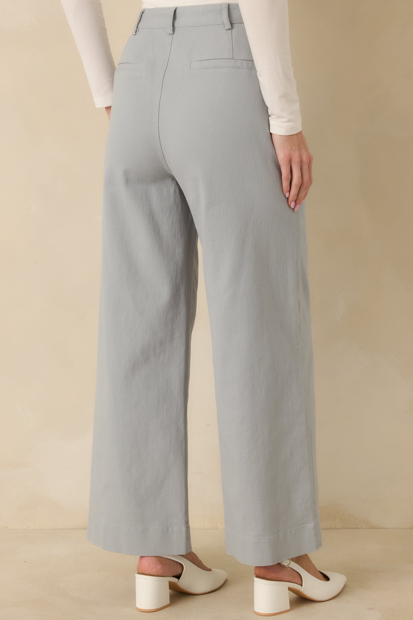 Rear view of dusty blue pants featuring back welt pockets and wide leg drape.