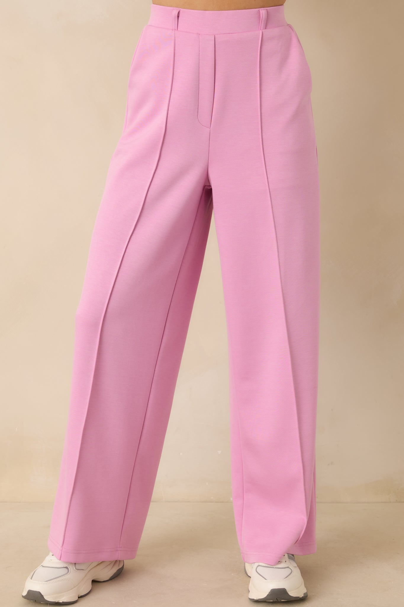Pink wide-leg pants highlighting the structured waistband with belt loops and tailored pleat detailing.