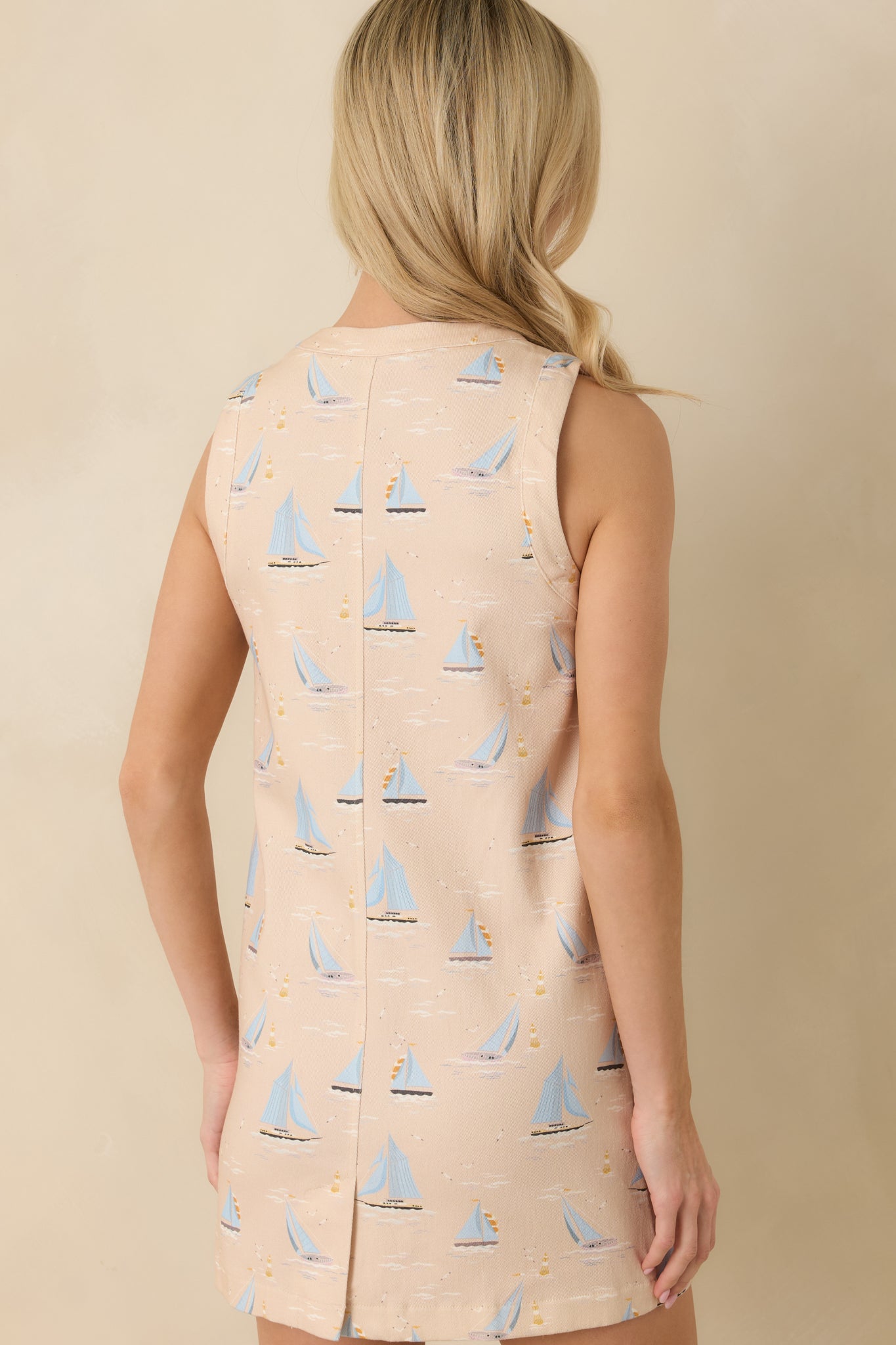 Light beige sleeveless mini dress displaying the relaxed mini-length silhouette from the rear with allover sailboat print.